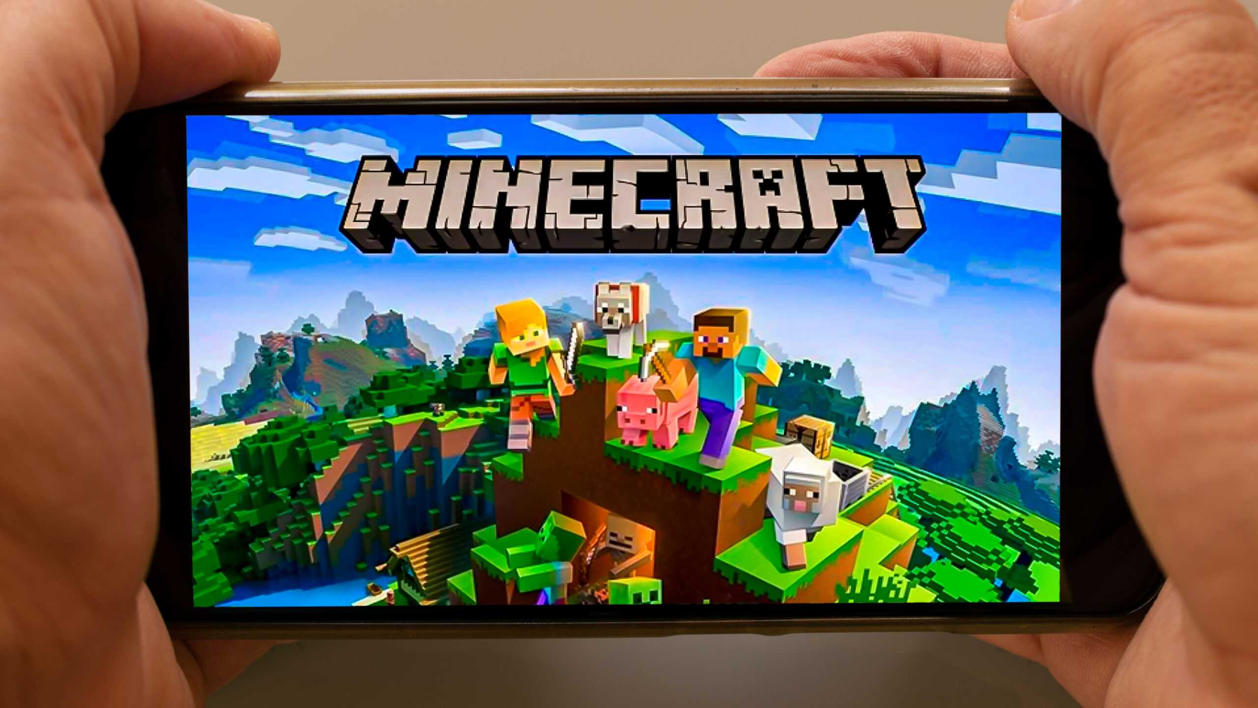 A person holding a smartphone displaying the game Minecraft, with characters and animals on a grassy block.